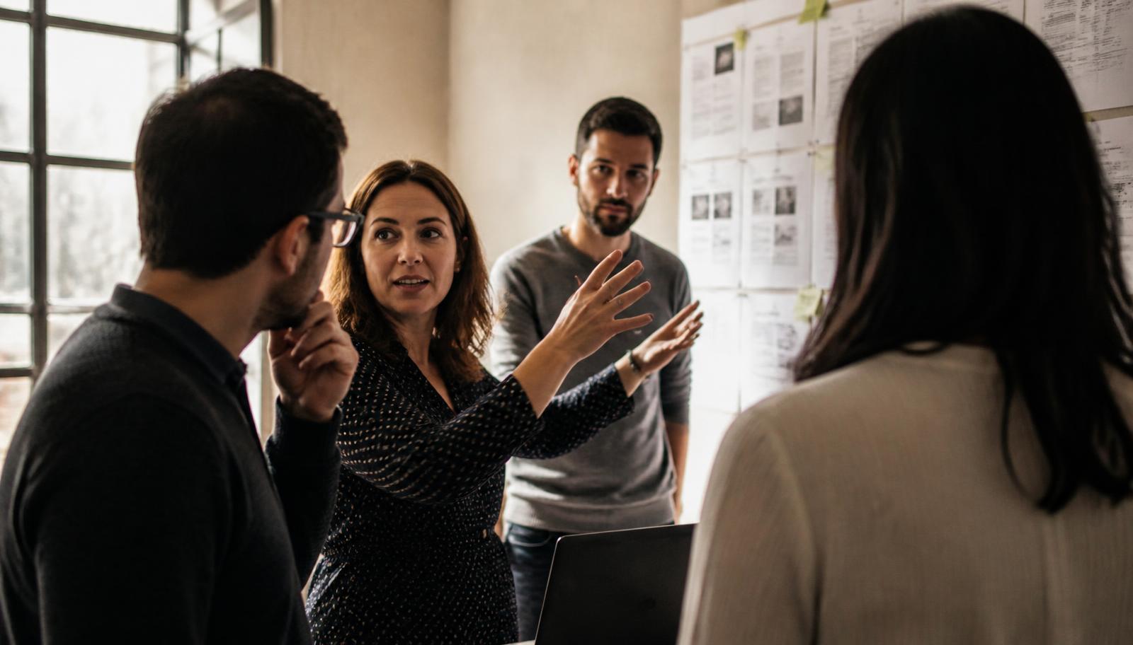 A sales manager coaching two reps beside a wall of printed call notes